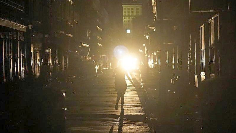 Eine Frau geht im Scheinwerferlicht eines patrouillierenden Polizeiwagens über die Bourbon Street in New Orleans. Foto: Eric Gay/AP/dpa