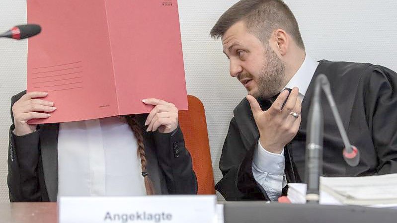 Die Angeklagte Jennifer W. hält im Gerichtssaal einen roten Aktendeckel vor das Gesicht. Rechts neben ihr sitzt Anwalt Ali Aydin. Foto: Peter Kneffel/dpa