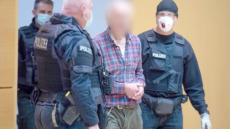 Der Angeklagte wird von einem Polizisten in den Verhandlungssaal geführt. Der Mann ist der Vater des Attentäters von Hanau. Foto: Boris Roessler/dpa