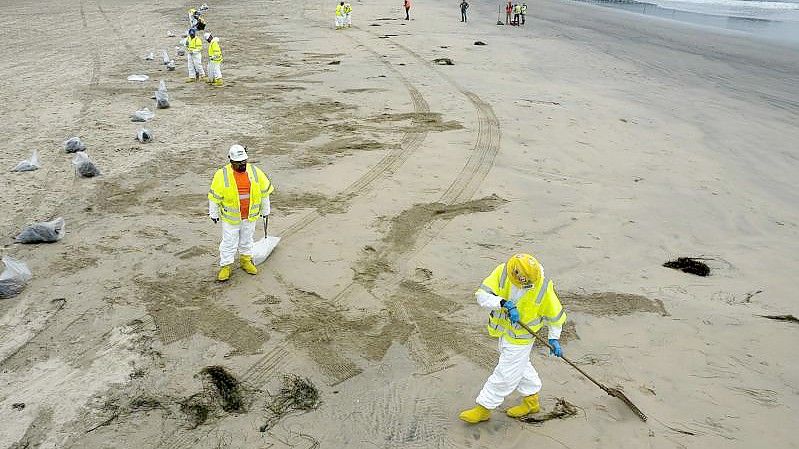 Arbeiter in Schutzanzügen reinigen den Strand nach einem Ölaustritt in Newport Beach, Kalifornien. Foto: Ringo H.W. Chiu/AP/dpa