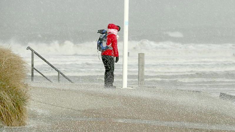 Eine Spaziergängerin blickt auf Norderney auf den Nordstrand und die Wellen der vom Sturm aufgepeitschten Nordsee, während ein Hagelschauer über sie heruntergeht. Foto: Volker Bartels/dpa