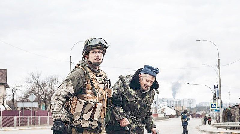 Ein ukrainischer Soldat in Irpin hilft einem älteren Mann, die Straße zu überqueren. Foto: Diego Herrera/EUROPA PRESS/dpa