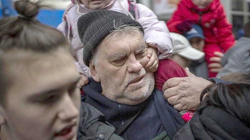 Ein Mädchen hält sich am Gesicht ihres Großvaters fest, während sie am Bahnhof von Kiew versuchen, in einen Zug nach Lwiw zu steigen. Foto: Emilio Morenatti/AP/dpa