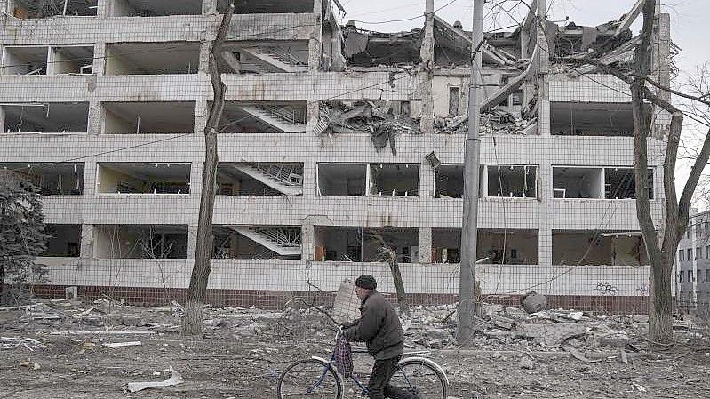 Ein Mann geht mit einem Fahrrad durch eine von Schutt übersäte Straße. Foto: Evgeniy Maloletka/AP/dpa