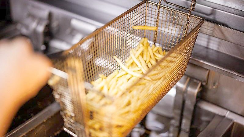 Eine Mitarbeiterin einer Münchener Filiale der Fastfoodkette McDonald's nimmt in einen Korb mit Pommes Frites aus der Friteuse. Foto: Matthias Balk/dpa