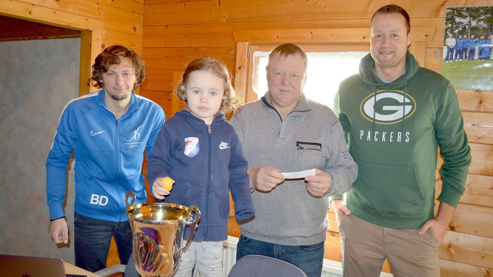 Die zweijährige Bella Dendzik durfte die Gruppenauslosung für den „Volksbank-Fehnpokal“ vornehmen. Ihr Vater Berti (links), Vorsitzender des Holter SV, sowie die Vorstandsmitglieder (von links) Günter und Thorsten Meyer schauten zu. Foto: Weers