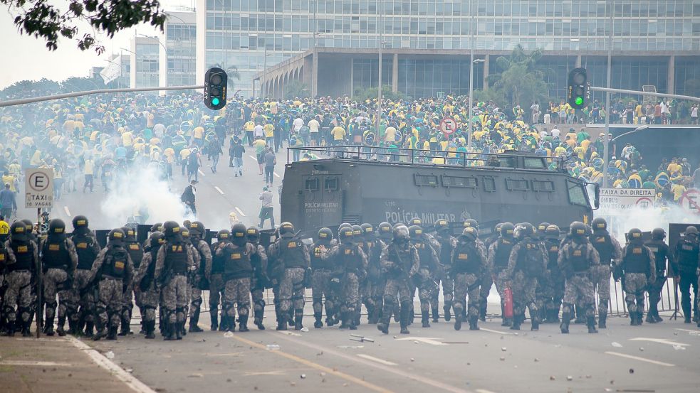 Anhänger des ehemaligen brasilianischen Präsidenten Bolsonaro stehen am Sonntag in Brasilia Ordnungskräften gegenüber, die hinter Absperrungen eine Kette bilden und Tränengasgranaten auf die Demonstranten abfeuern. Foto: Alves/DPA