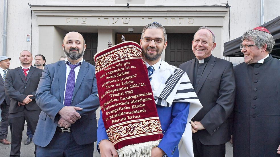 Jüdisches Leben in Deutschland: Alexander Nachama (2.v.l.), Landesrabbiner der Jüdischen Landesgemeinde Thüringens, Sofer Rabbiner Reuven Yaacobov (l), Ulrich Neymeyr (2.v.r.), Bischof des katholischen Bistums Erfurt, und Friedrich Kramer (r), Landesbischof der Evangelischen Kirche in Mitteldeutschland (EKM) stehen mit der neuen Torarolle für die jüdische Landesgemeinde vor der Synagoge. Foto: picture alliance/dpa/dpa-Zentralbild