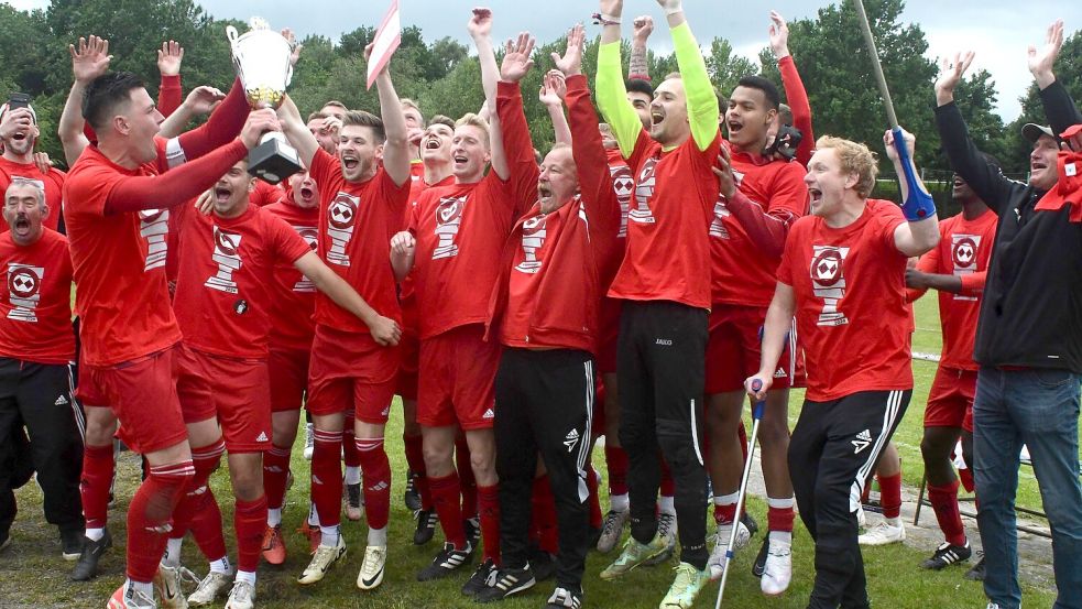 Uplengens Kapitän Julian Marchlewitz stemmt den Pokal vor den jubelnden Mitspielern in die Höhe. Foto: Damm