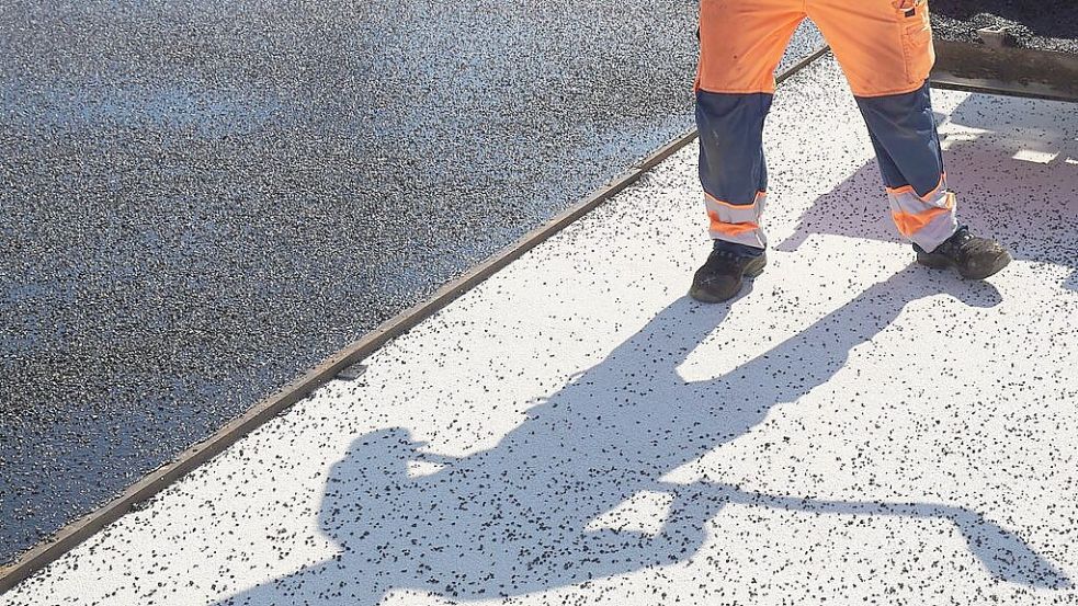 Der Schatten eines Bauarbeiters fällt auf den Boden einer Straße, die asphaltiert wird. Im Bezirk der Straßenmeisterei Friesoythe werden Fahrbahnen und Radwege saniert. Symbolfoto: DPA