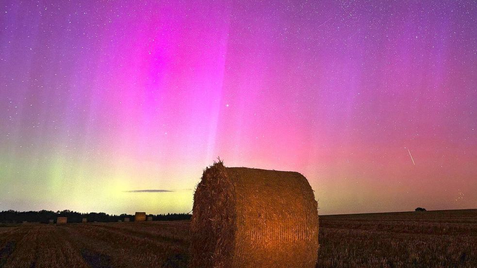 Nordlichter am Himmel, während eine Sternschnuppe über einem Strohballen am Himmel verglüht. Foto: Georg Moritz/dpa