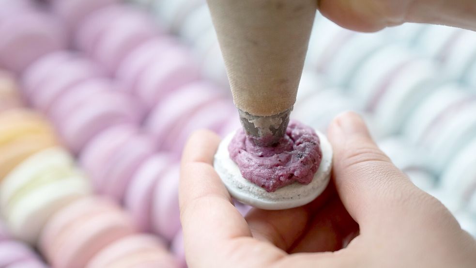 Das Baisergebäck Macaron wird in einer Bäckerei mit einer Spritztüte befüllt. (Archivbild) Foto: Sebastian Kahnert/dpa