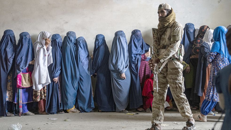 Ein Taliban-Kämpfer steht Wache, während Frauen in Kabul, Afghanistan, darauf warten, Lebensmittelrationen zu erhalten, die von einer humanitären Hilfsgruppe verteilt werden. Foto: dpa/Ebrahim Noroozi