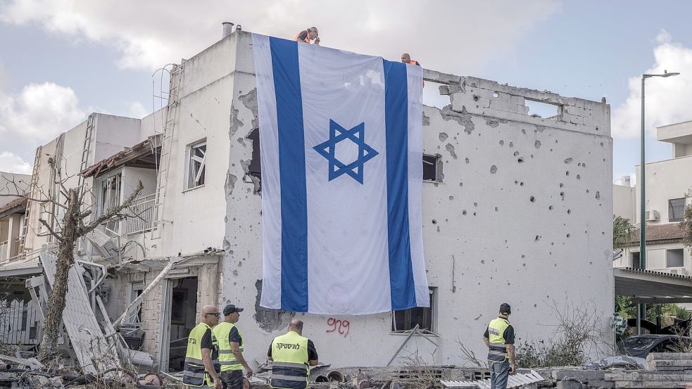 Eine riesige israelische Fahne hängt vom Dach eines beschädigten Gebäudes in Kiriat Bialik. Foto: Ilia Yefimovich/dpa