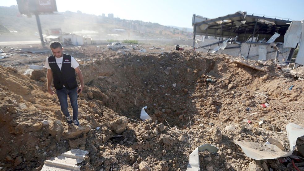 Ein libanesischer Polizist steht in der Nähe eines Kraters nach einem israelischen Luftangriff auf einen Hangar im Südlibanon. Foto: Mohammed Zaatari/AP/dpa