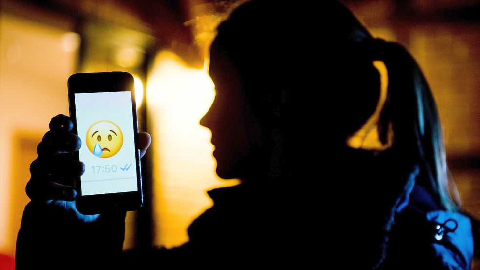 Ein junges Mädchen zeigt das Display eines Smartphones mit einem weinenden Emoji bem Messenger „WhatsApp“. Foto: Stratenschulte