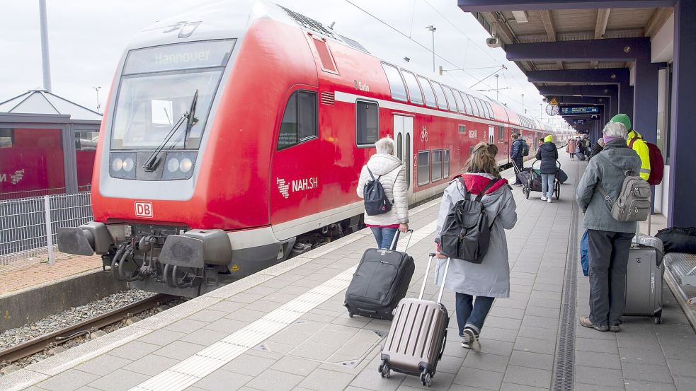 Touristen laufen mit Rollkoffern am Bahnhof Norddeich-Mole entlang. Die Linie dorthin über Leer und Emden ist für die Tourismusbranche von großer Bedeutung. Foto: Dulian/DPA