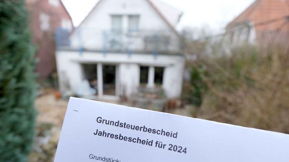 Ein Grundsteuerbescheid für 2024 wird vor einem Privatgrundstück hochgehalten. Die Grundsteuererhebung wurde reformiert, weil sie auf veralteten Daten basiert hatte. Der Rat der Gemeinde Barßel legte den neuen Hebesatz bei 270 Prozent fest. Bisher lagen die Hebesätze bei 370 Prozent. Foto: Weißbrod/DPA