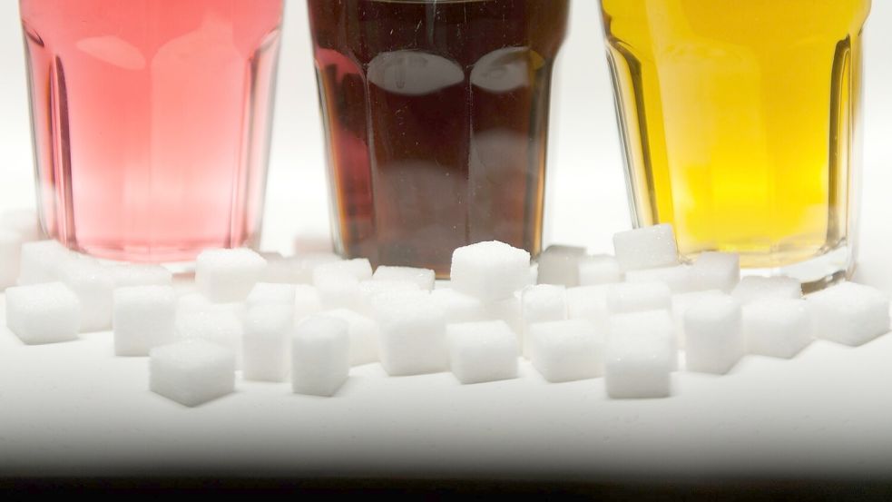 Drei Gläser gefüllt mit roter Limonade, Cola und einem Energy-Drink neben Zuckerwürfeln auf einem Tisch Foto: Monika Skolimowska/dpa