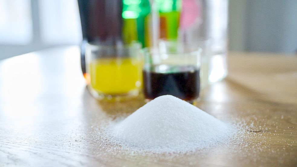 Drei unterschiedliche Arten Softdrinks und die Flaschen dazu stehen auf einem Tisch, während ein Berg von Zucker davor aufgeschüttet ist Foto: Annette Riedl/dpa