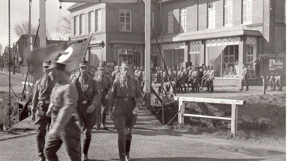 Das Foto zeigt einen Aufmarsch in Westrhauderfehn. Der Anlass und das Datum für die Aufnahme sind nicht bekannt. Im Hintergrund ist das Geschäft Hagius zu sehen.