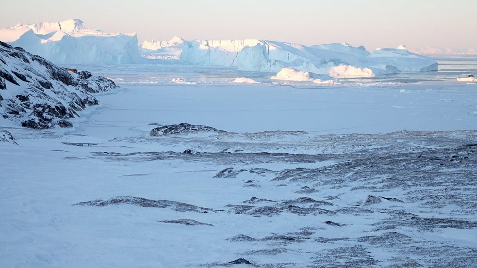 Eisberge ragen im Ilulissat-Eisfjord hinter einer verschneiten Gesteinslandschaft in die Höhe. Foto: Steffen Trumpf/dpa