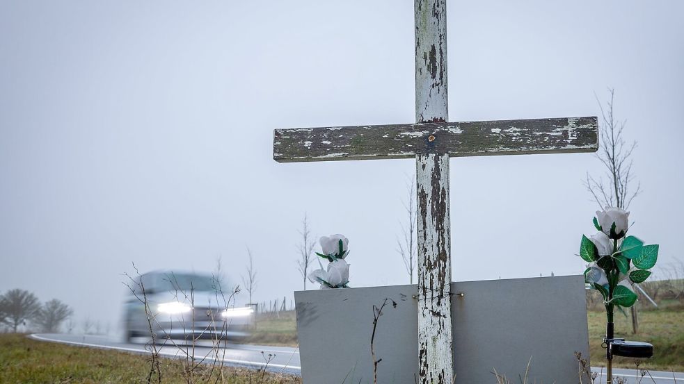 in Auto fährt auf einer Landstraße an einem hölzernen Kreuz vorbei, welches zur Erinnerung an ein Unfallopfer aufgestellt wurde. Foto: Jens Büttner/dpa